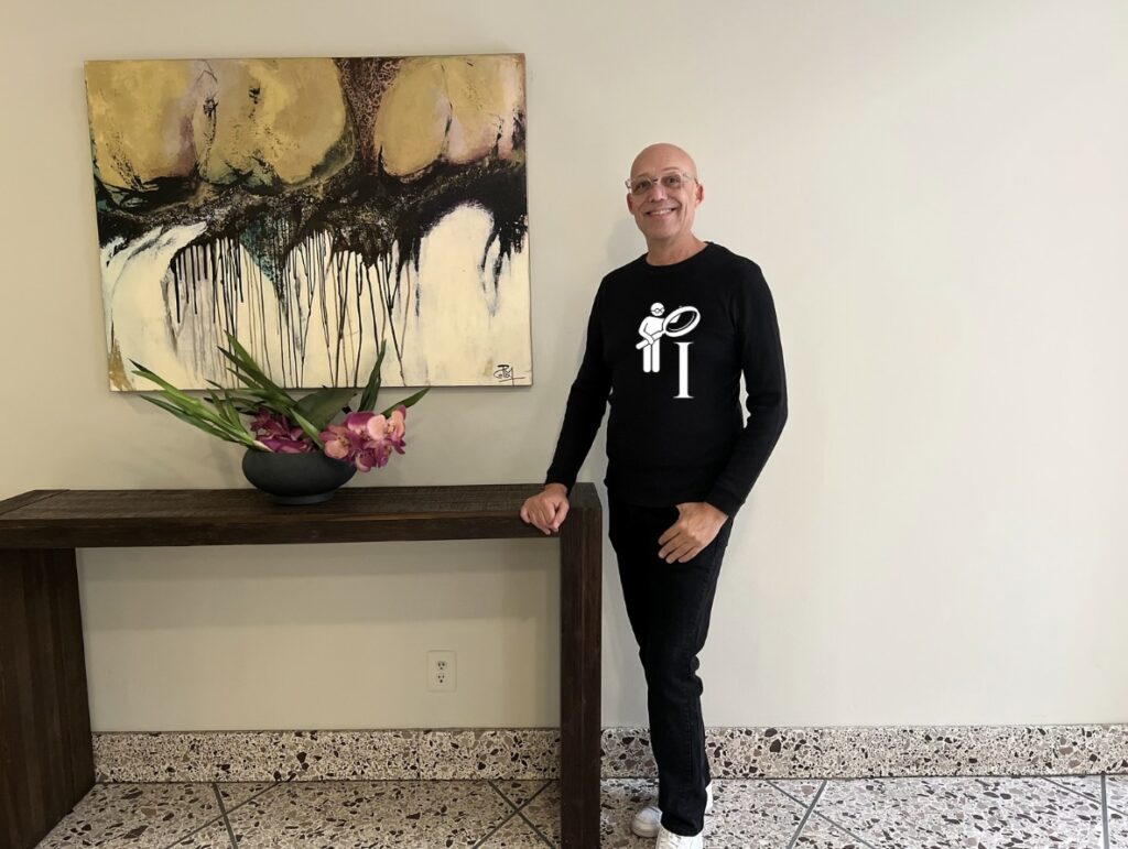 Todd is a fair skin black male, shaved head, clear framed glasses, bright blue eyes is modeling the Focus on the "I" black long sleeve shirt. I has an image in white of a person icon holding a large magnifying glass over a capital letter "I"